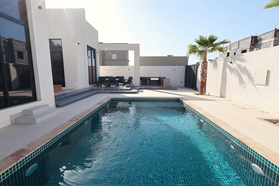 A rectangular swimming pool with mosaic lining, deck and palms, project A29