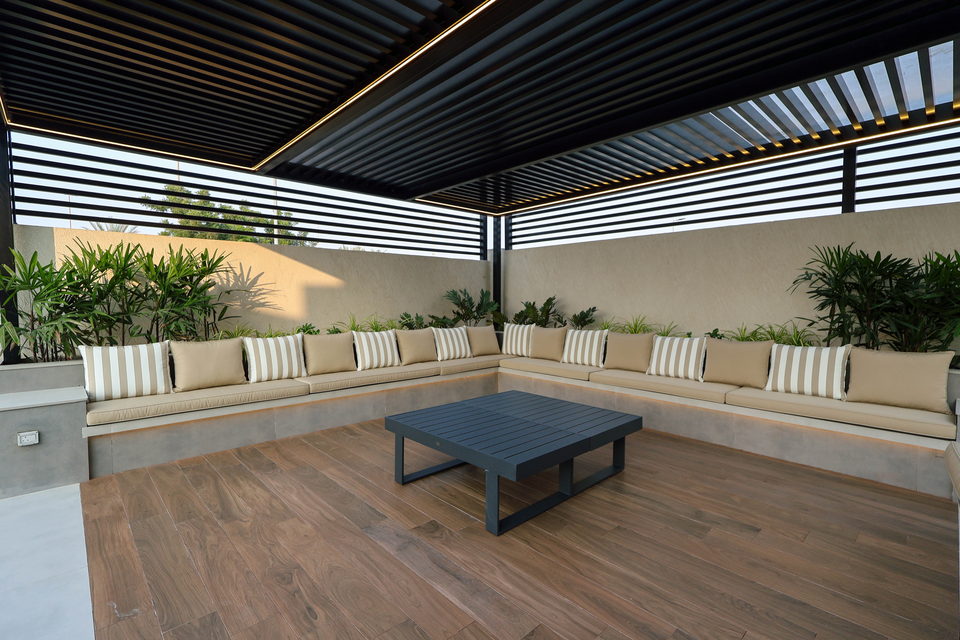A covered outdoor lounge with cushioned bench seating and timber decking, project A49
