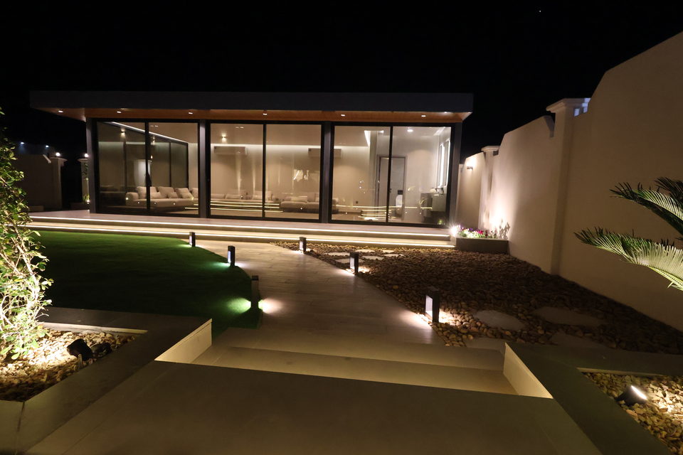 A lit glass majlis with full-height glazing opening onto a lawn at dusk, project R43 in Ras Al Khaimah